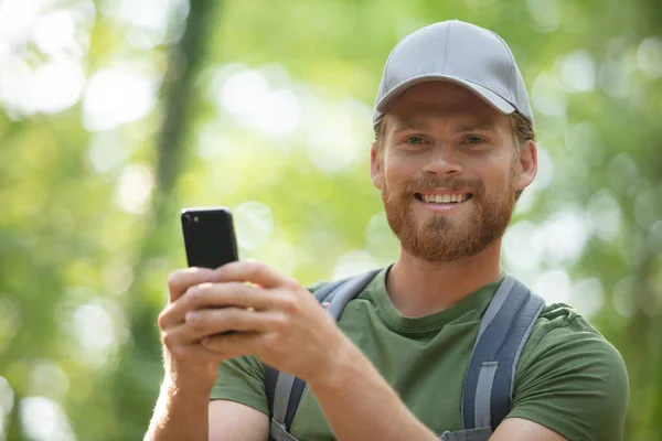 男子徒步旅行者在秋天的森林里用智能手机拍照 — 图库照片