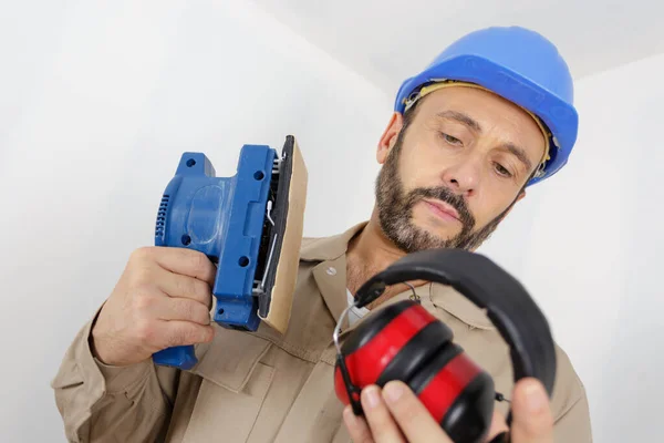 Construtor Considerando Usar Auriculares Enquanto Estiver Usando Lixadeira — Fotografia de Stock
