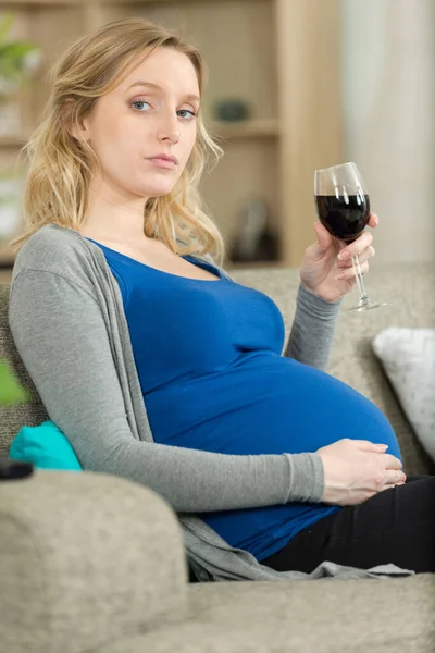 妊娠中の女性がワインを飲みながらソファに座って — ストック写真