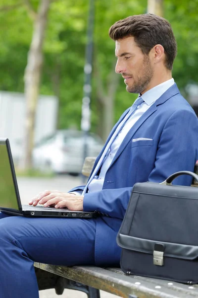 商人坐在长椅上 一边用笔记本电脑 — 图库照片