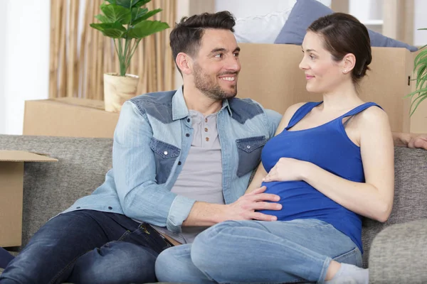 一个快乐的男人在沙发上摸着一个微笑的孕妇的肚子 — 图库照片