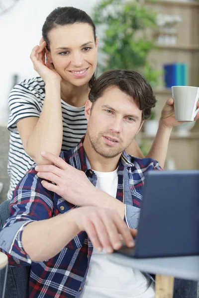 笑着的年轻夫妇用笔记本电脑在沙发上放松 — 图库照片