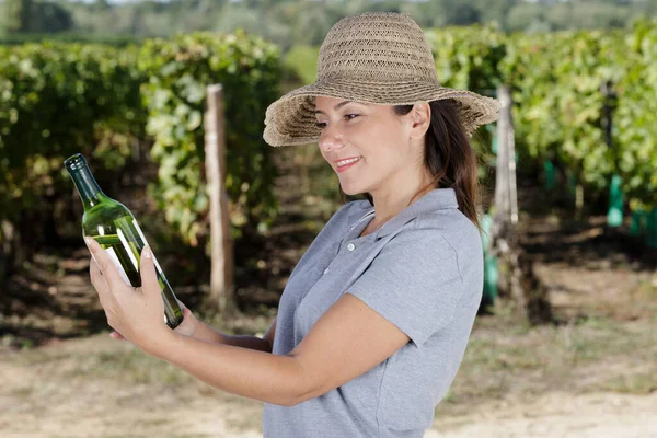 ブドウ畑でワインボトルを見ている女性は — ストック写真