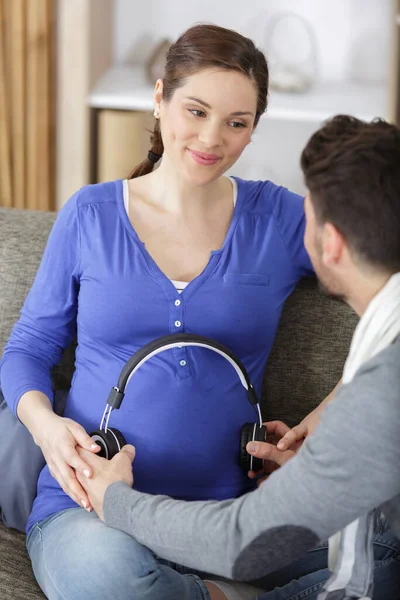 妊婦さんとご主人はヘッドフォンで音楽を演奏しています — ストック写真