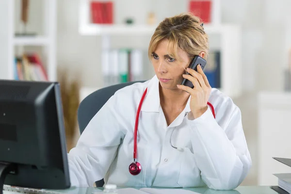 Médico Femenino Mediana Edad Teléfono Mientras Mira Ordenador —  Fotos de Stock