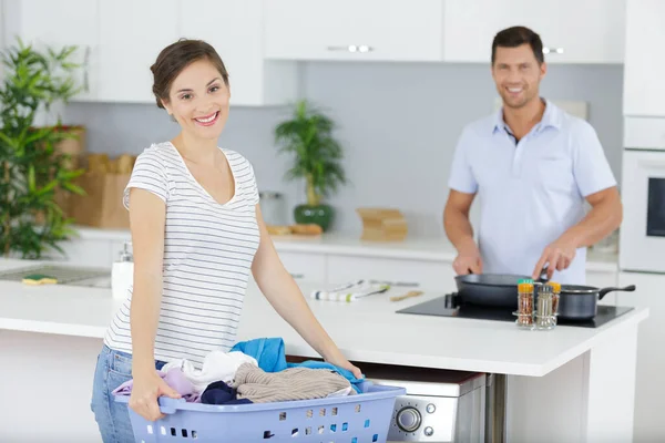 女人在丈夫做饭的时候做洗衣房 — 图库照片