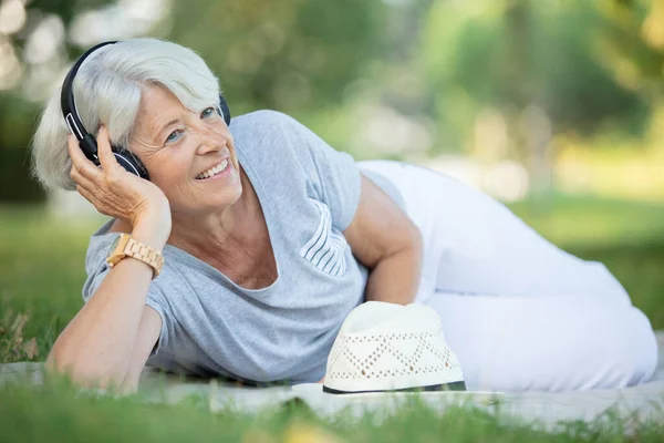 Atraktivní Seniorka Používající Sluchátka Trávě — Stock fotografie