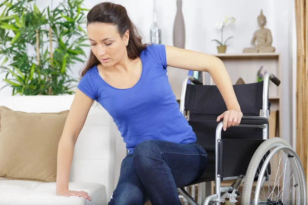 坐轮椅移动到沙发上的残疾妇女 — 图库照片