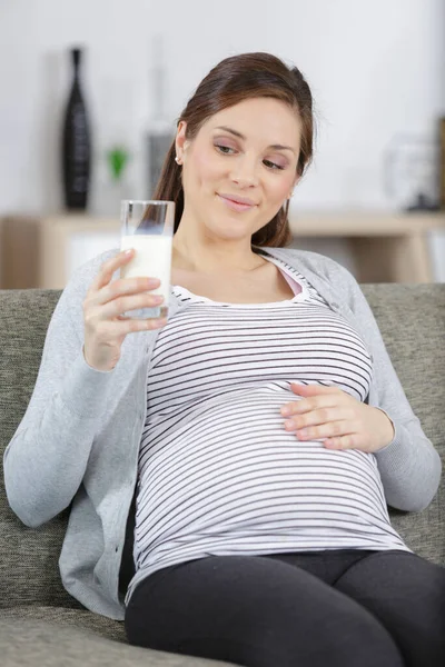 年轻孕妇与牛奶和早餐在沙发上 — 图库照片