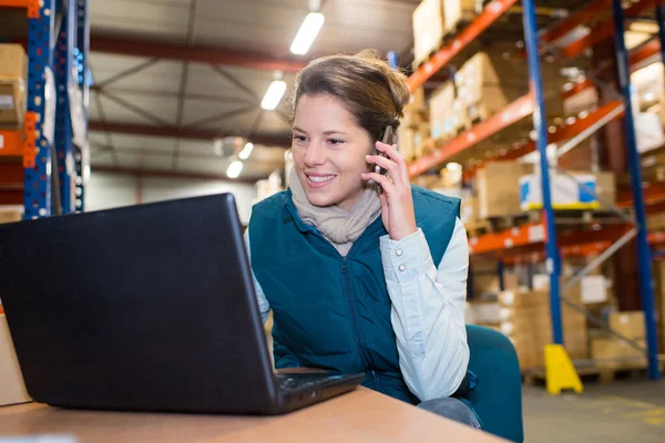 warehouse manager using telephone and laptop in a large warehouse