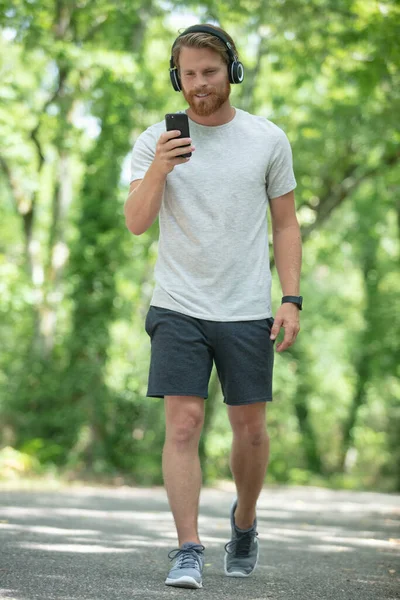 Hombre Caminando Con Auriculares Mirando Teléfono Inteligente —  Fotos de Stock