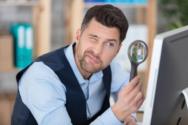man looking at computer through a magnifying glass