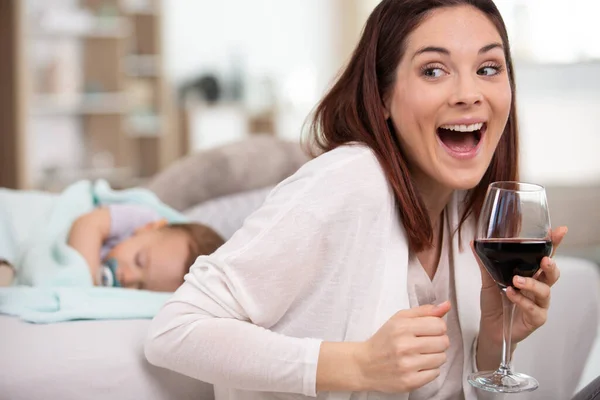 mother drinking glass of wine in front of sleeping baby