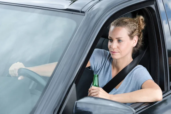 若い女性ドライバーが運転中にビールを飲んでいます — ストック写真