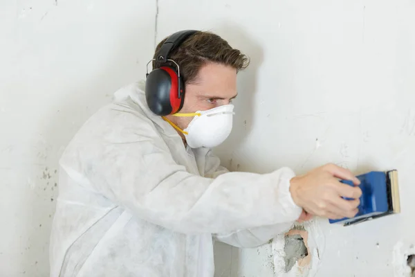 worker after sanding wall wearing mask