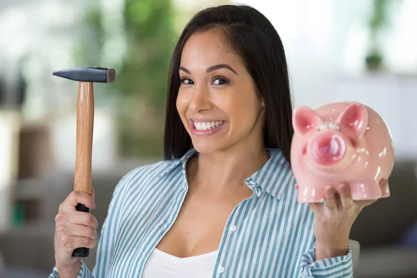 smiling woman holding hammer and pink piggy bank