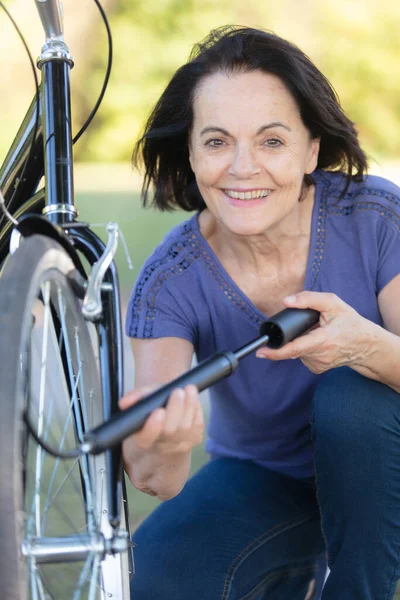 老年妇女给自行车车轮打气 — 图库照片