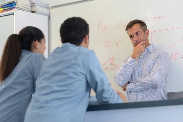 teacher standing while math lesson in front of a blackboard
