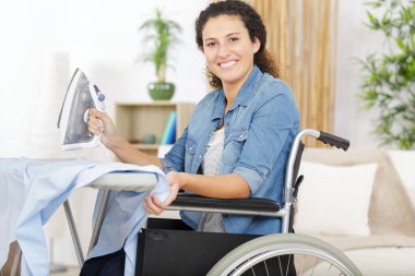 happy woman in a wheelchair ironing at home clipart