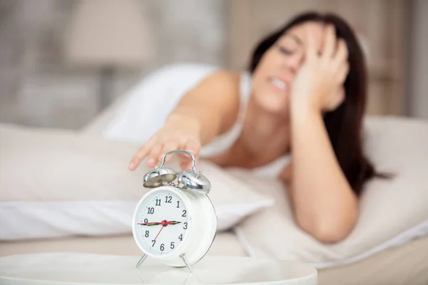 young sleepy woman turning alarm clock off