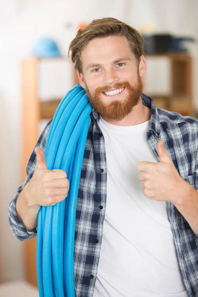 tradesman holding roll of blue pipe with thumbs up