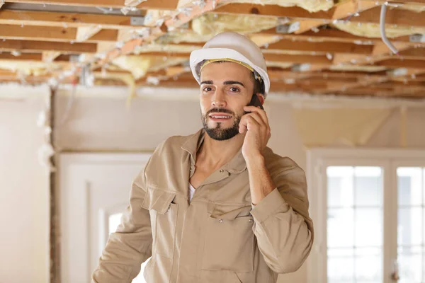 young male builder using smartphone in renovation property