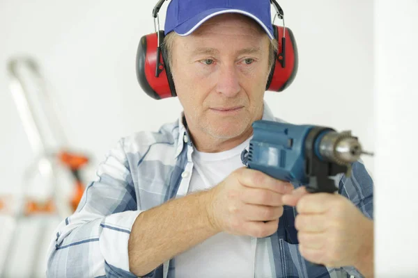 senior workman using drill and wearing ear-defenders