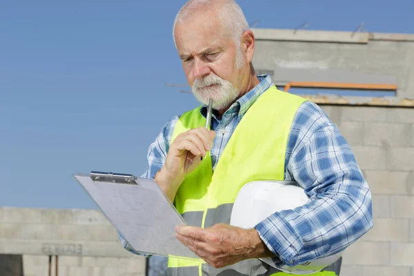 senior engineer builder checking clipboard at construction site