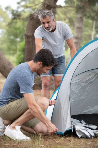 young man and older friend putting up a tent