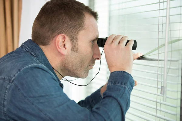 man looking through window with binoculars