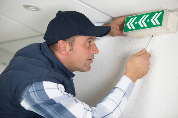 a male worker fixing an emergency exit sign