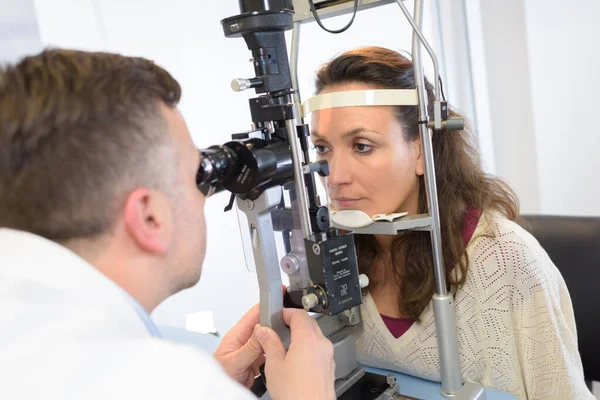 拡大装置を通して患者の目を調べる光科学者 — ストック写真