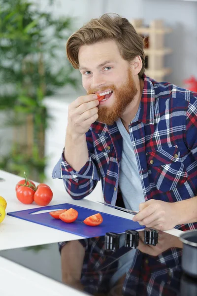 男人在家里做饭的时候吃西红柿 — 图库照片