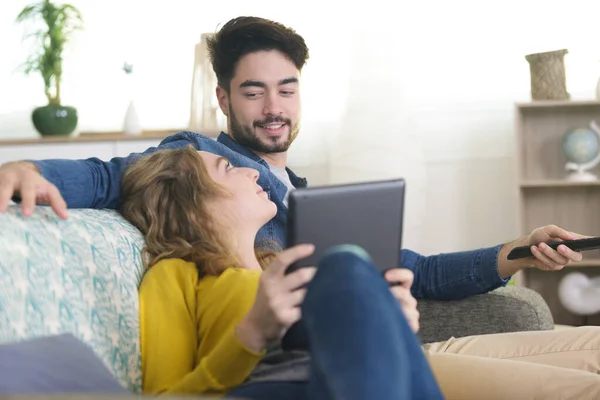 Ζευγάρι Χαλαρώνοντας Στον Καναπέ Χρησιμοποιώντας Tablet Και Βλέποντας Τηλεόραση — Φωτογραφία Αρχείου