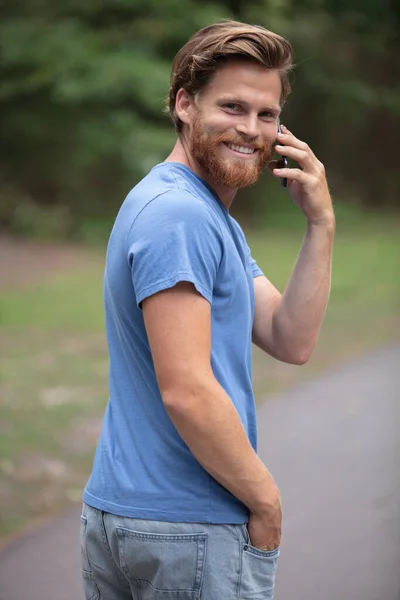 Άντρας Που Περπατάει Στο Πάρκο Χαμογελώντας Στο Τηλέφωνο — Φωτογραφία Αρχείου