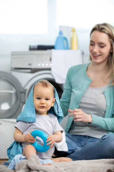 mother with baby play with laundry in utility room