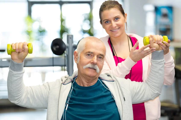 physiotherapist assisting senior man to lift dumbbell in clinic