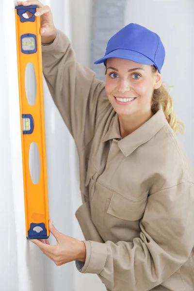 笑着做硬帽的女建筑工人用水平工具做测量 — 图库照片