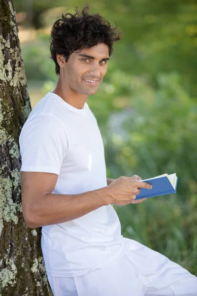 若いリラックスした男が木の上で本を読む — ストック写真
