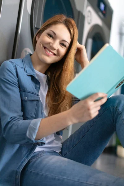 Happy Young Woman Reading Book Laundromat — Stock Photo, Image