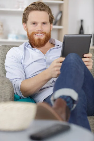Schöner Glücklicher Mann Der Auf Dem Sofa Auf Tablette Schaut — Stockfoto