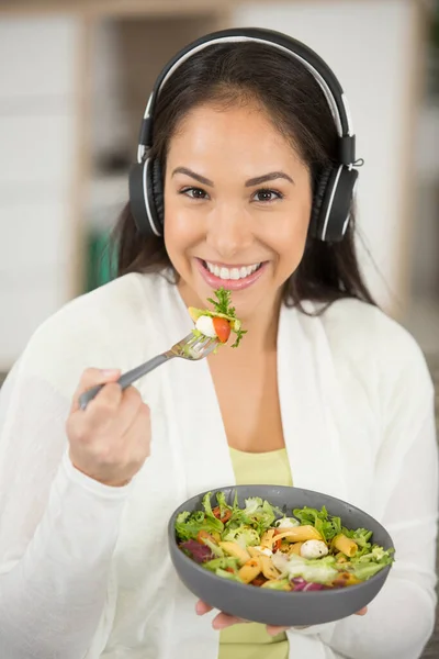 woman listening to music with headphones while eating salad