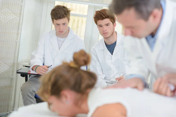 医者が患者の背中に働くのを見ている学生 — ストック写真