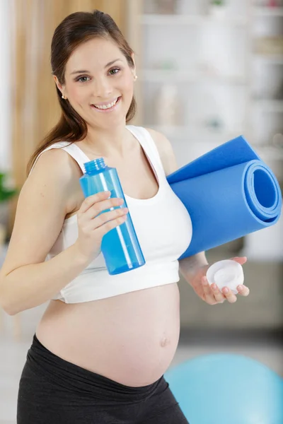妊娠中の女性は運動マットと水のボトルを持って — ストック写真