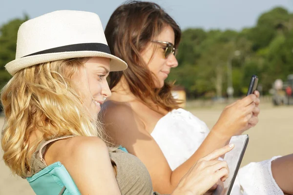 两名年轻女士在海滩上使用电子设备 — 图库照片