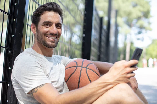 微笑的篮球运动员坐着看电话 — 图库照片