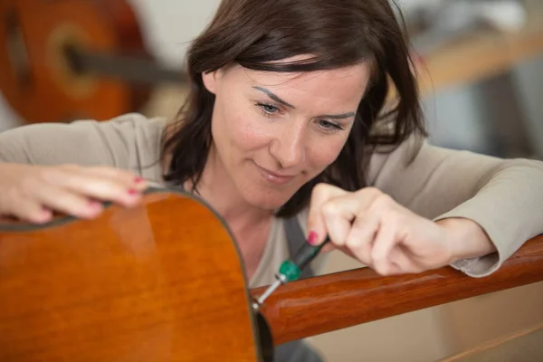 woman repairing a guitar with screwdriver