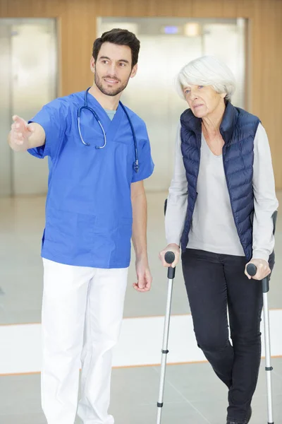 若い男性医師と話す松葉杖を持つ老婦人 — ストック写真