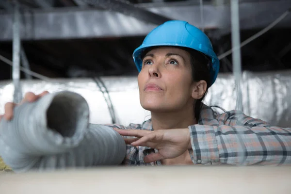 天井にエアコン用のパイプを取り付ける女性電気技師は — ストック写真
