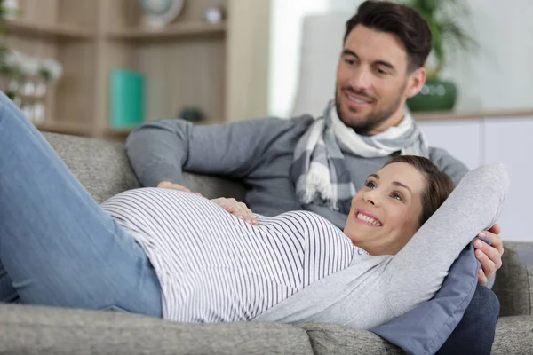 怀孕的年轻夫妇躺在家里的沙发上 — 图库照片